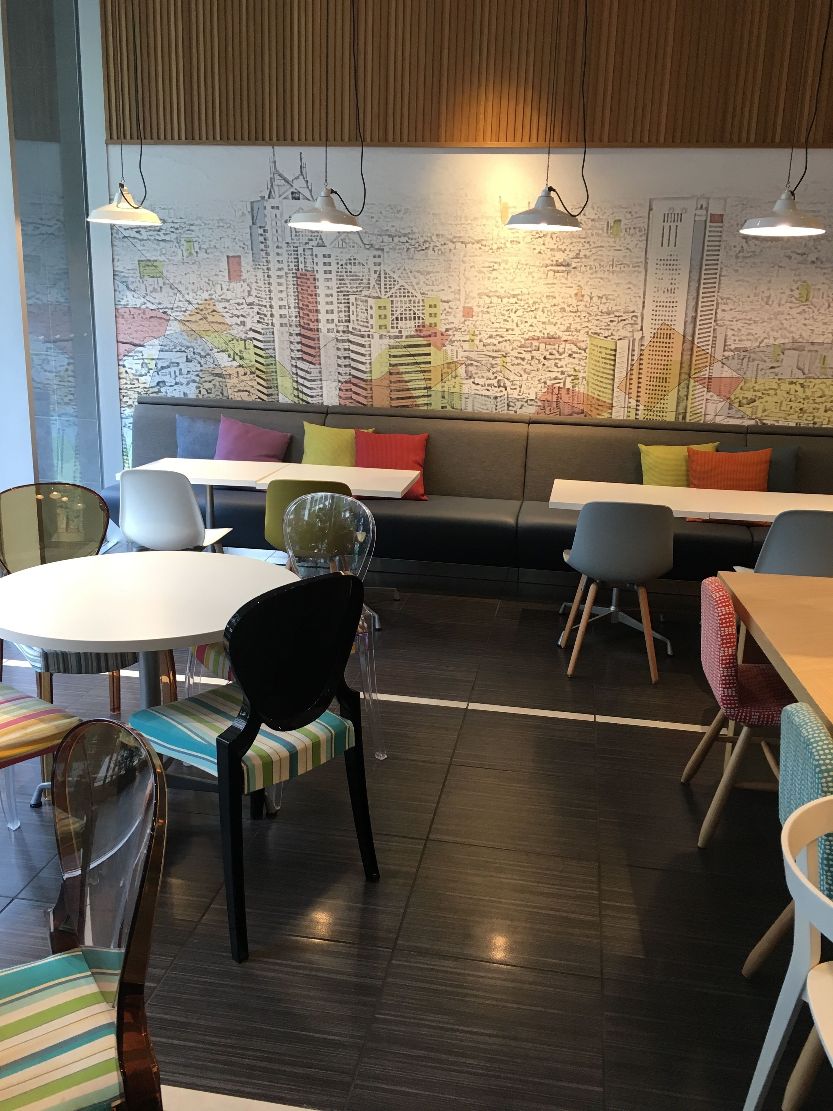 Un café moderno con un mural de paisaje urbano, una variedad de opciones de asiento, incluyendo un sofá y sillas, e iluminación colgante.
