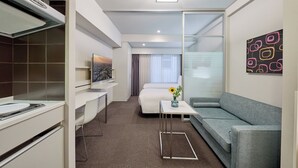 A modern hotel room with a kitchenette, a bed, a sofa, a small table with a vase, and a painting on the wall. - Citadines Shinjuku Tokyo (Tokyo)