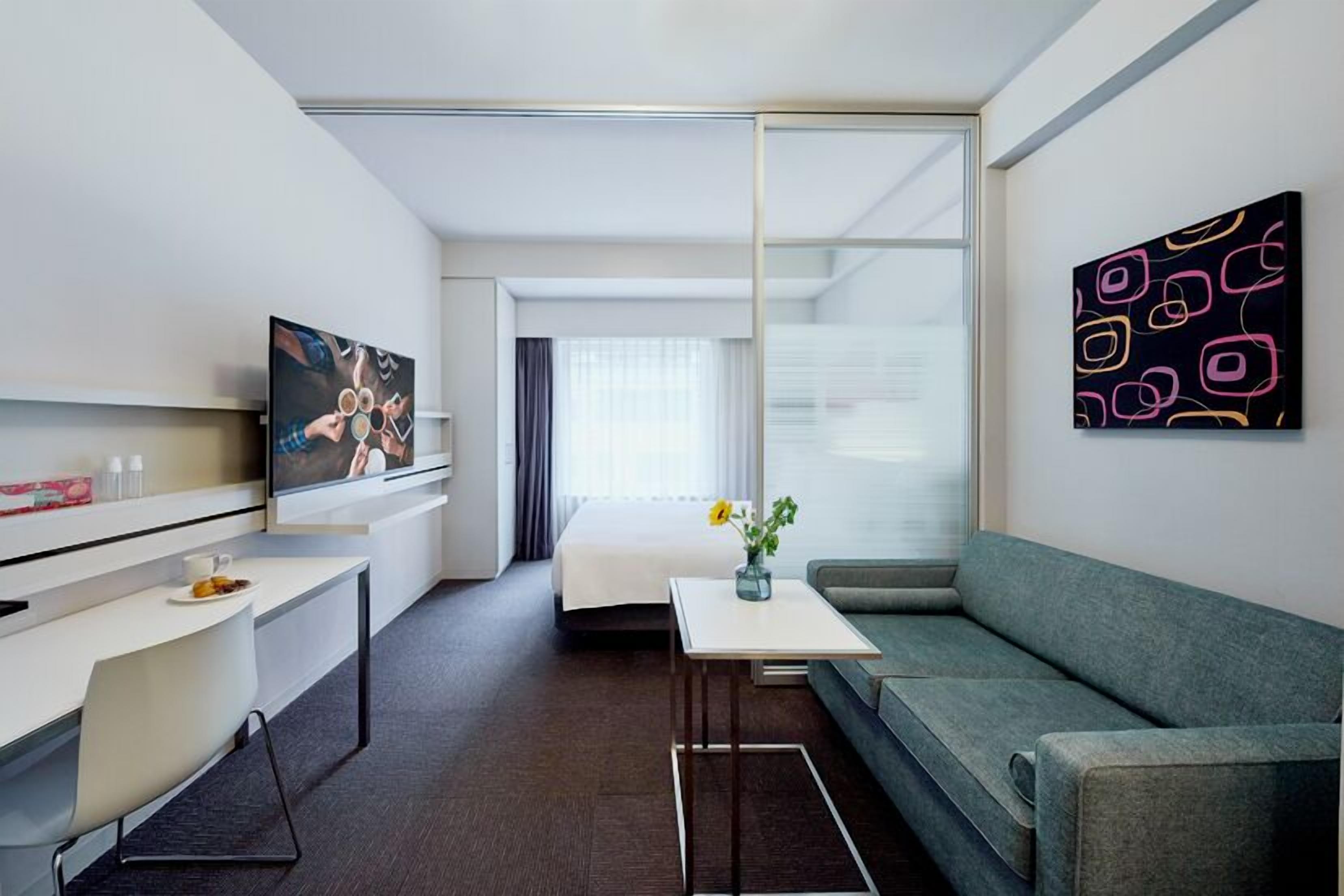A modern hotel room with a sofa, a small table, a TV, and a painting on the wall.