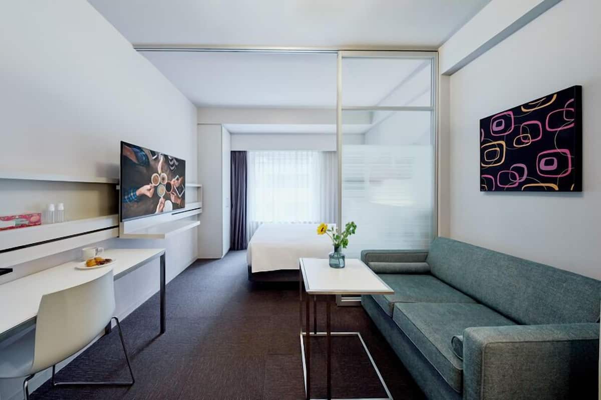 Ein modernes Hotelzimmer mit einer Couch, einem kleinen Tisch, einem Fernseher und einem Bild an der Wand.