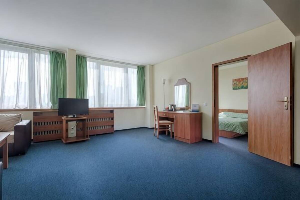 A hotel room with a bed, a desk, a chair, a TV, a dresser, and a door.
