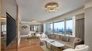 A spacious living room with a large sofa, a coffee table, and a dining area with a kitchen in the background. - Titanic Port Bakirkoy (Istanbul)