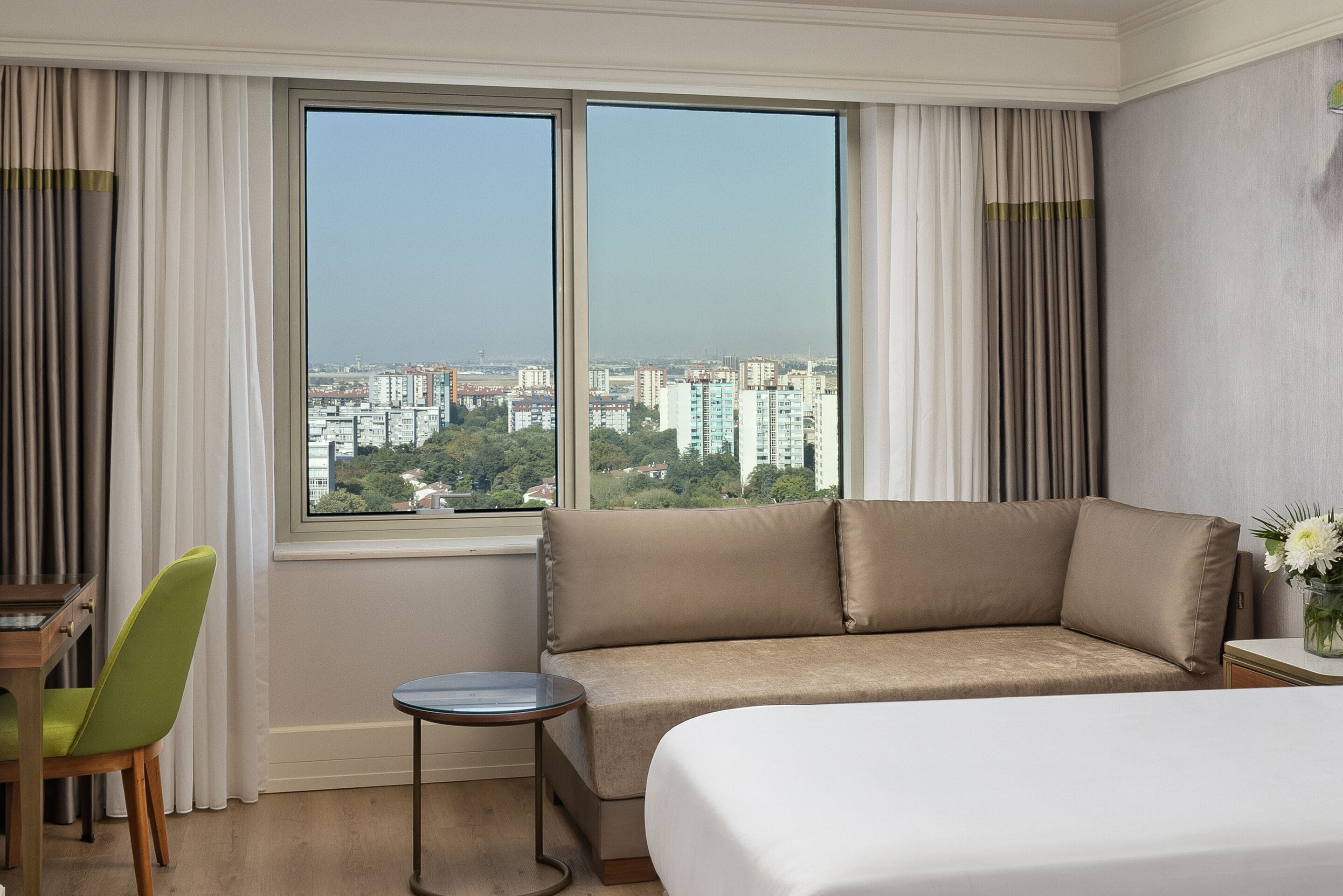 A hotel room with a large window, a sofa, a small round table, and a bed.