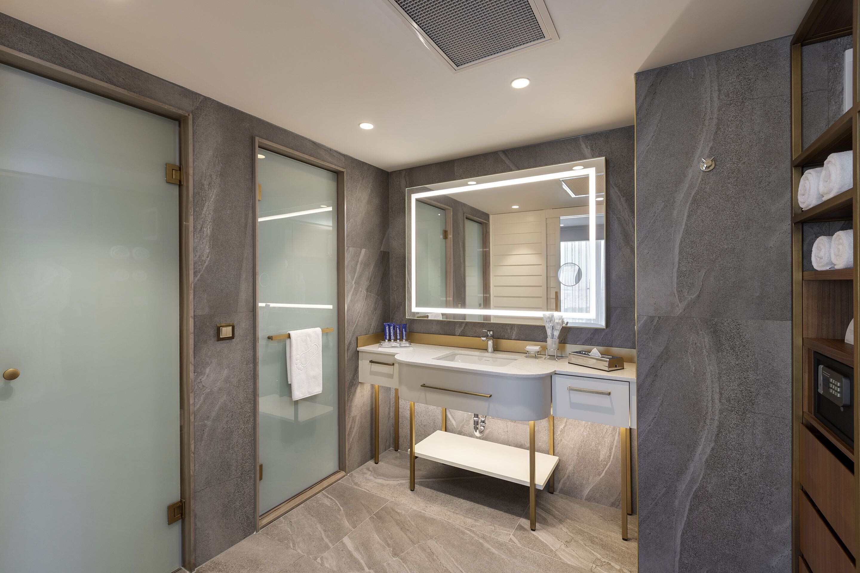 A modern bathroom with a glass shower enclosure, a vanity with a large mirror, and a built-in towel rack.