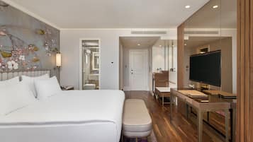 Quarto de hotel moderno com uma cama grande, uma escrivaninha, televisão e banheiro visível por uma porta aberta.
