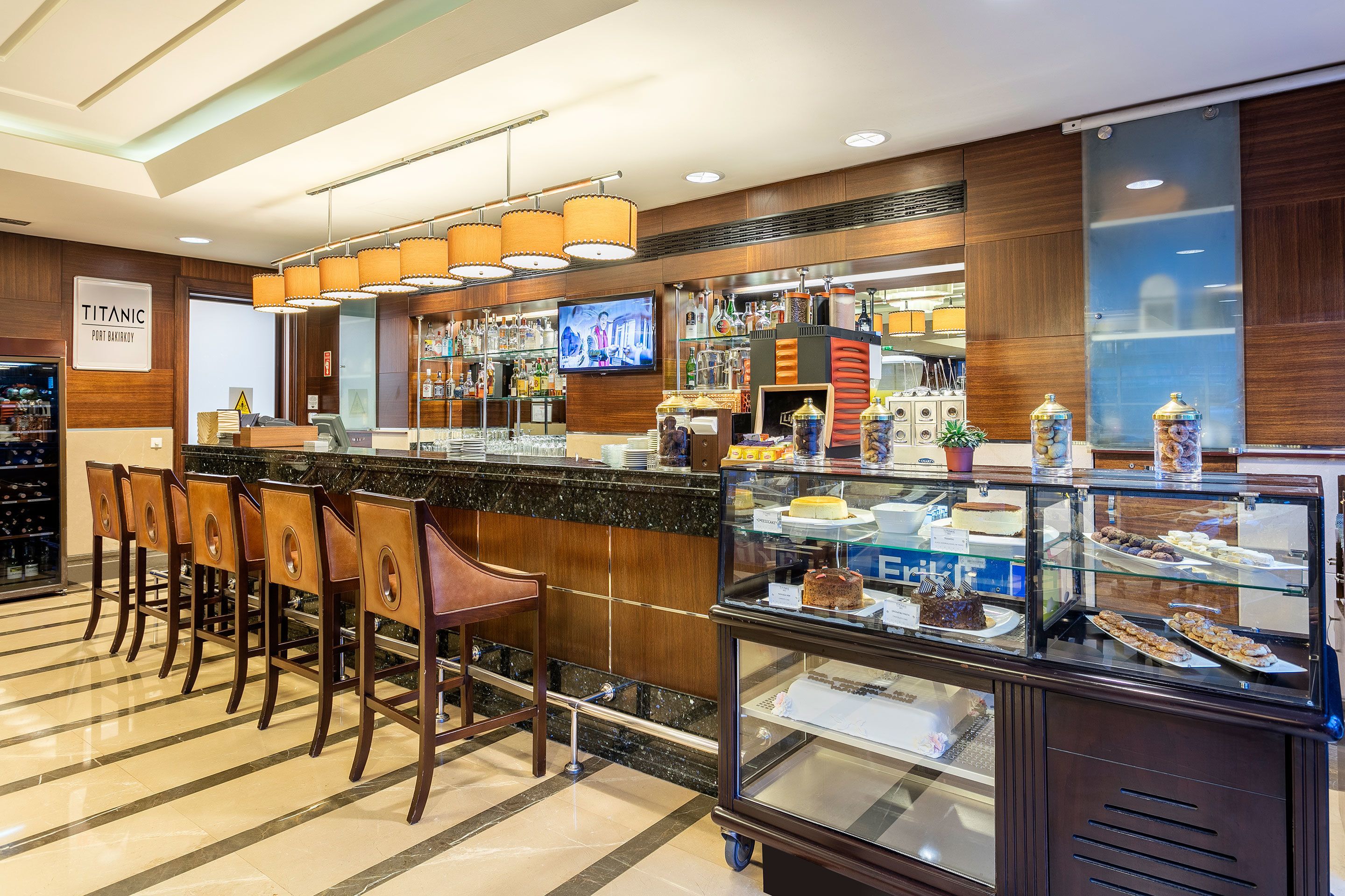 Een bar met een toonbank, barkrukken, een televisie en een vitrine met desserts.
