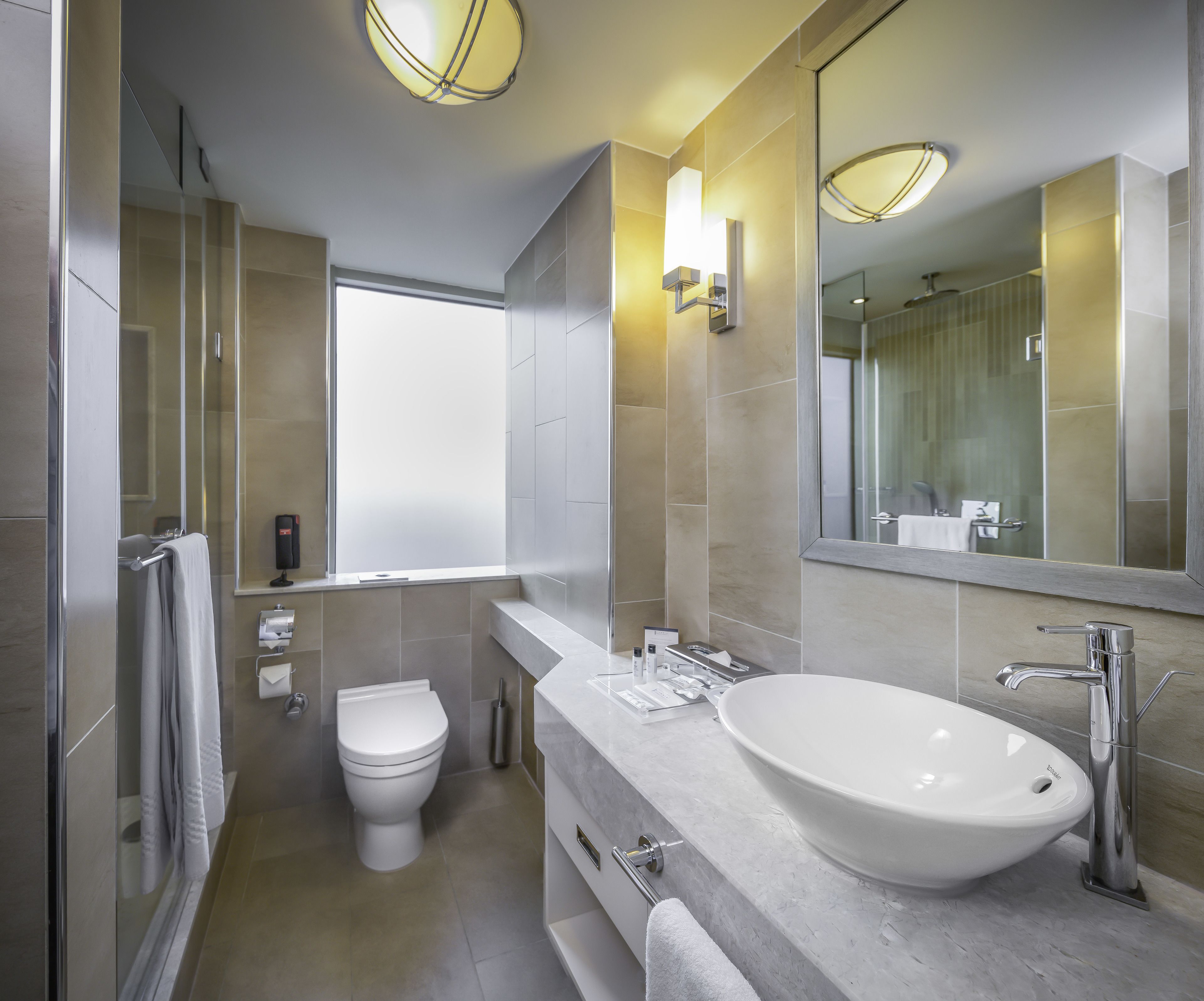 A modern bathroom with a large mirror, a white sink, and a toilet.