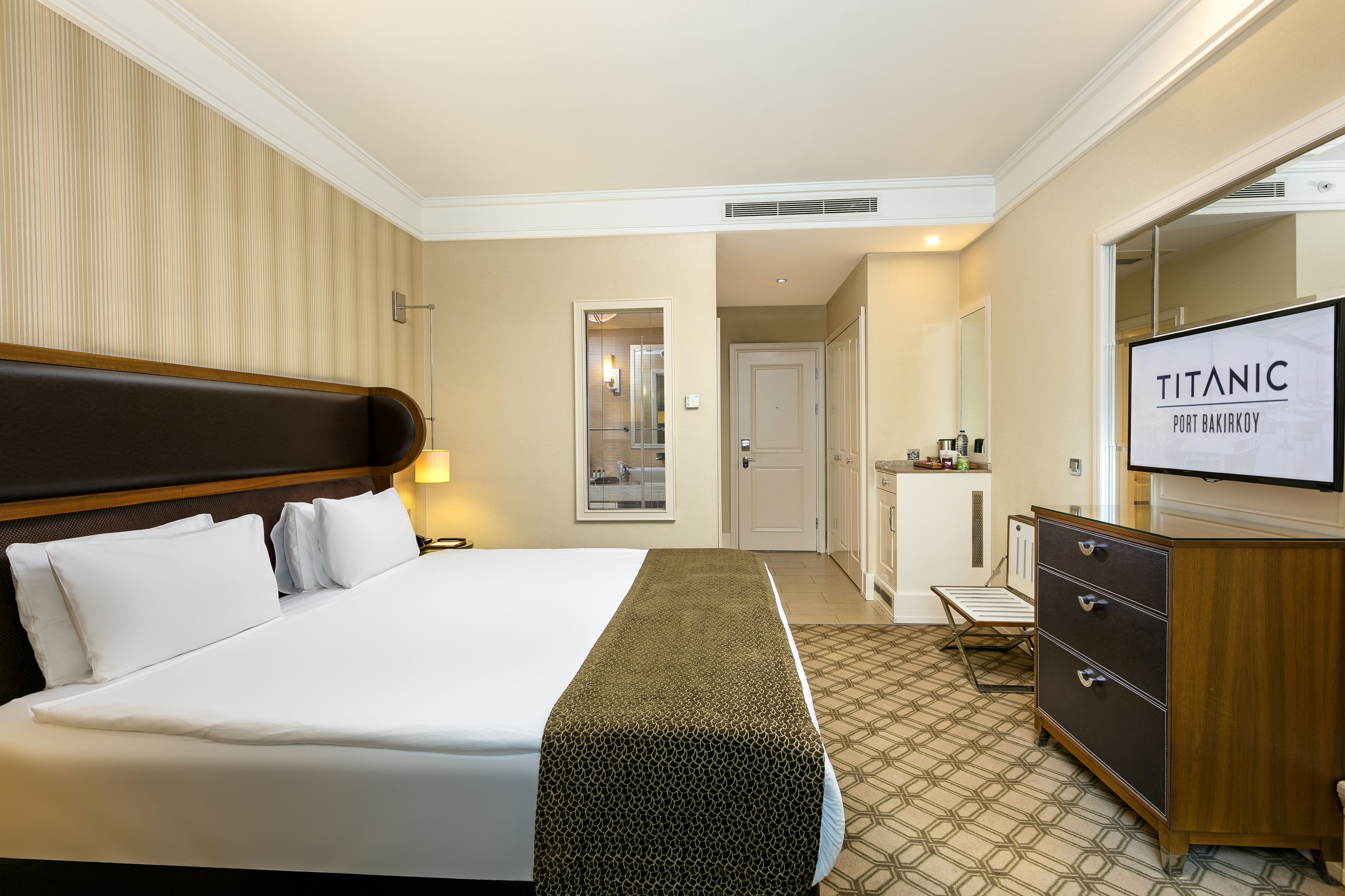 Une chambre d’hôtel avec un grand lit, une commode, une télévision et une porte donnant sur une salle de bain.