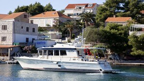 Ein weißes Boot namens "BLÁŽA" liegt an einem Jachthafen fest, im Hintergrund ist ein Restaurant namens "RESTAURANT" zu sehen.