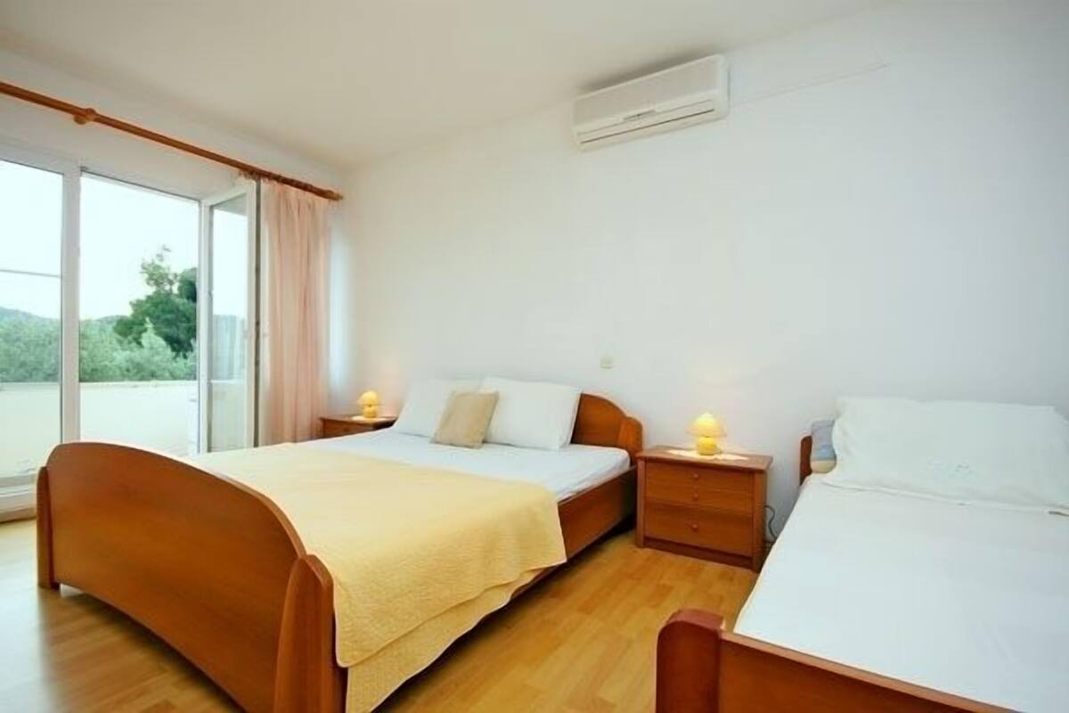A bedroom with two beds, a large window, and an air conditioning unit.