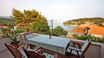 A terrace with a checkered table and chairs, overlooking a coastal area with houses and trees.