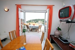 Un área de comedor con una mesa y sillas de madera, una planta pequeña en maceta y un televisor sobre un mueble.