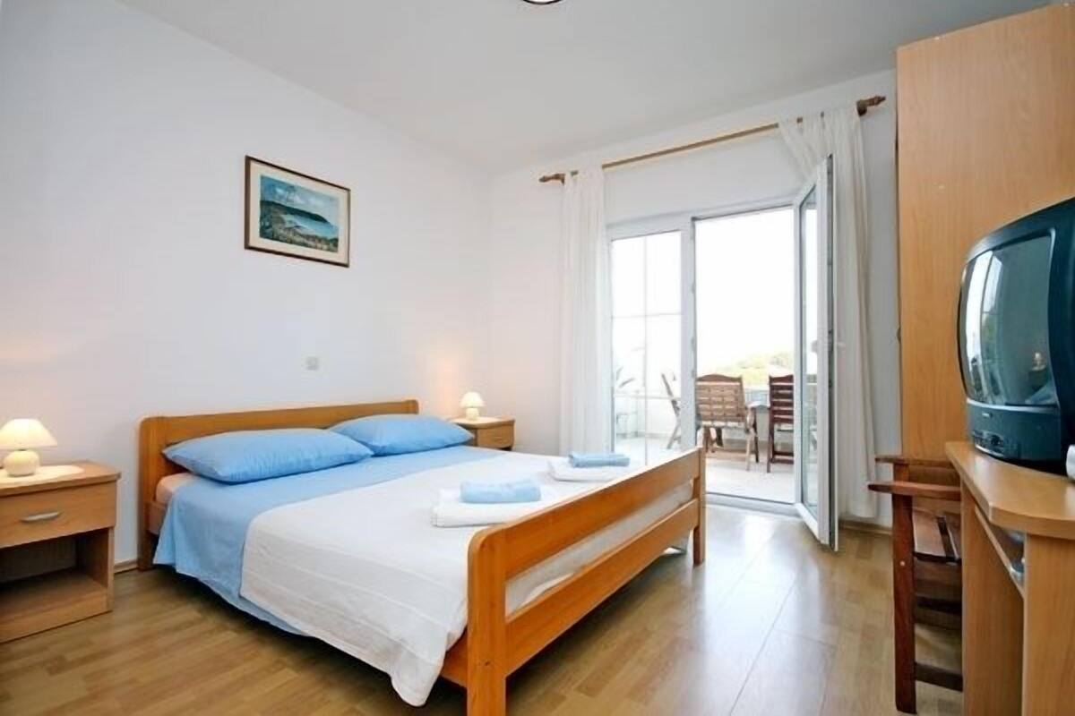 A bedroom with a wooden bed, a television, and a view of the outdoors through a sliding glass door.