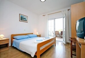 Un dormitorio con una cama de madera, un televisor y vistas al exterior a través de una puerta corrediza de vidrio.