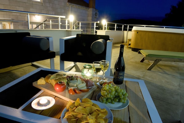 Una terraza en la azotea con una mesa preparada para una comida, que incluye una variedad de quesos, frutas y aperitivos.