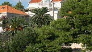 Ein Gebäude mit rotem Ziegeldach, umgeben von üppiger Vegetation und einer Steinmauer.