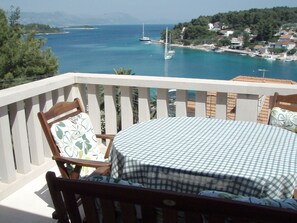 Un balcón con mesa y sillas a cuadros, con vistas a una zona costera con barcos y casas.