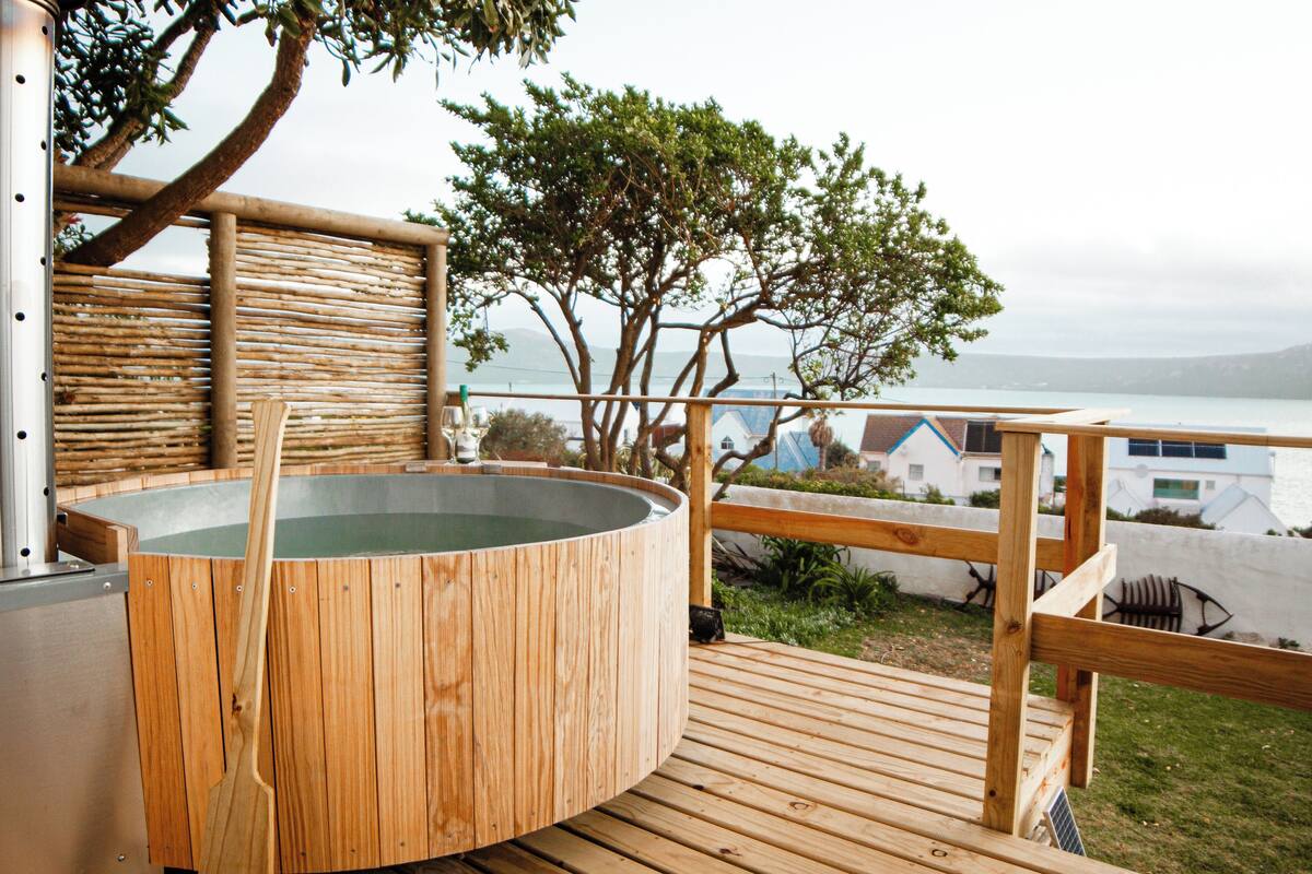 A wooden deck with a hot tub, a wooden fence, and a view of the sea.