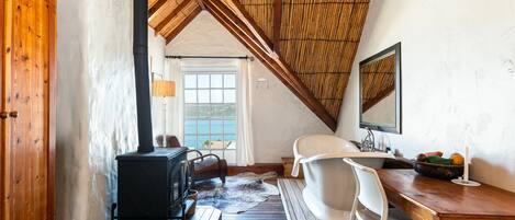 A cozy room with a wooden ceiling, a black stove, a white chair, and a wooden desk.