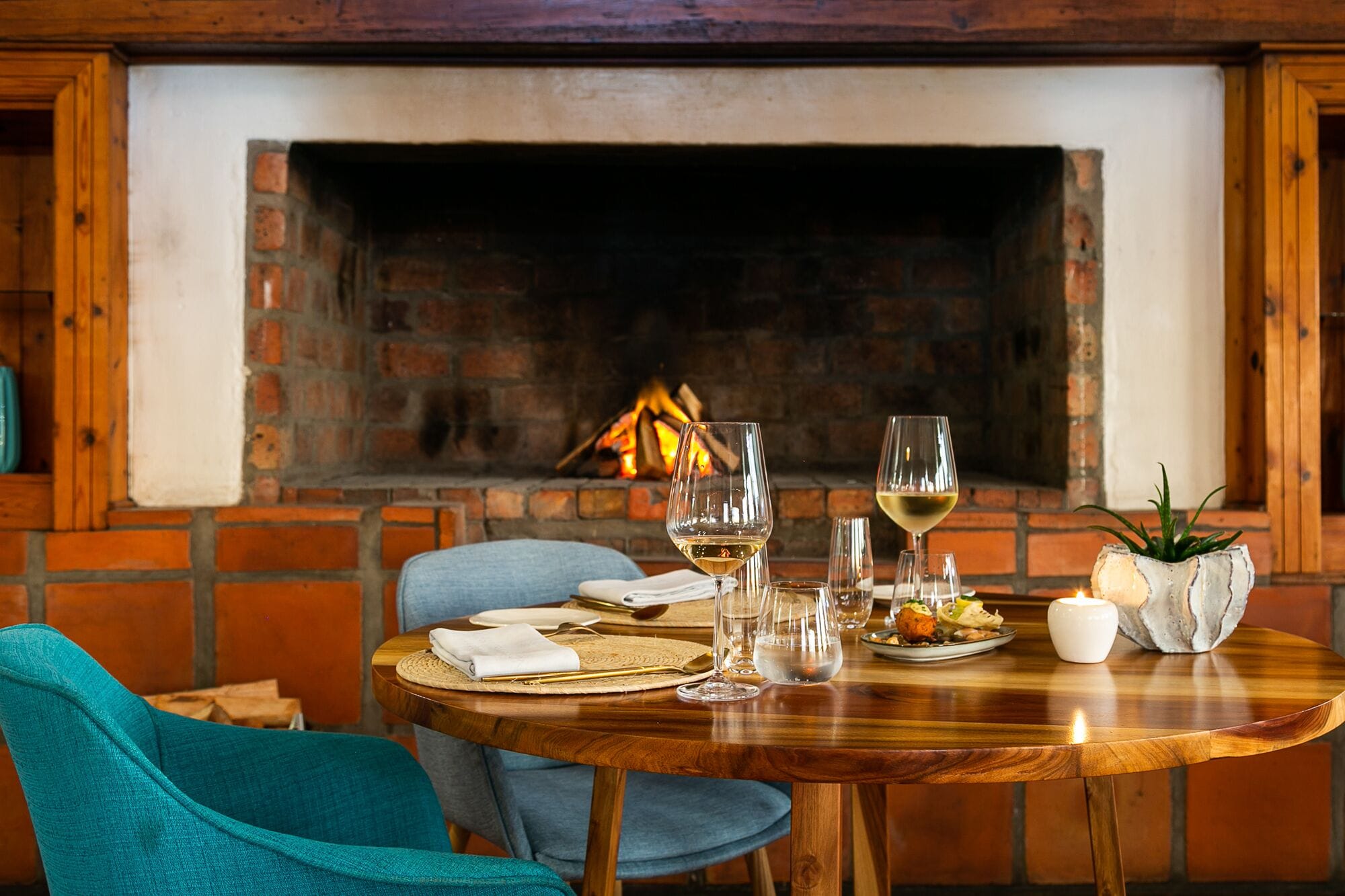 A dining table set for two with a fireplace in the background.