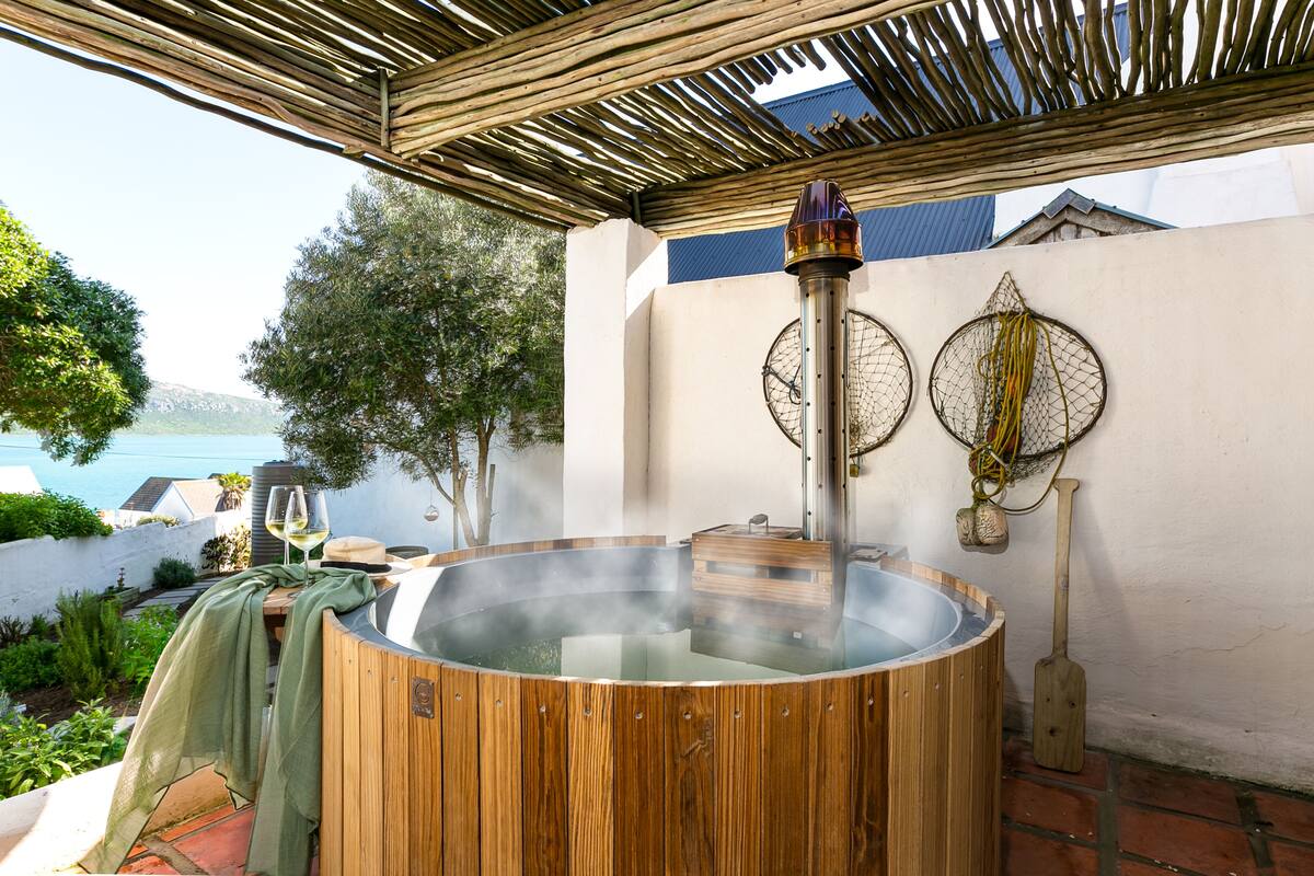 A hot tub with a wooden exterior, a wooden roof overhead, and a view of the sea.