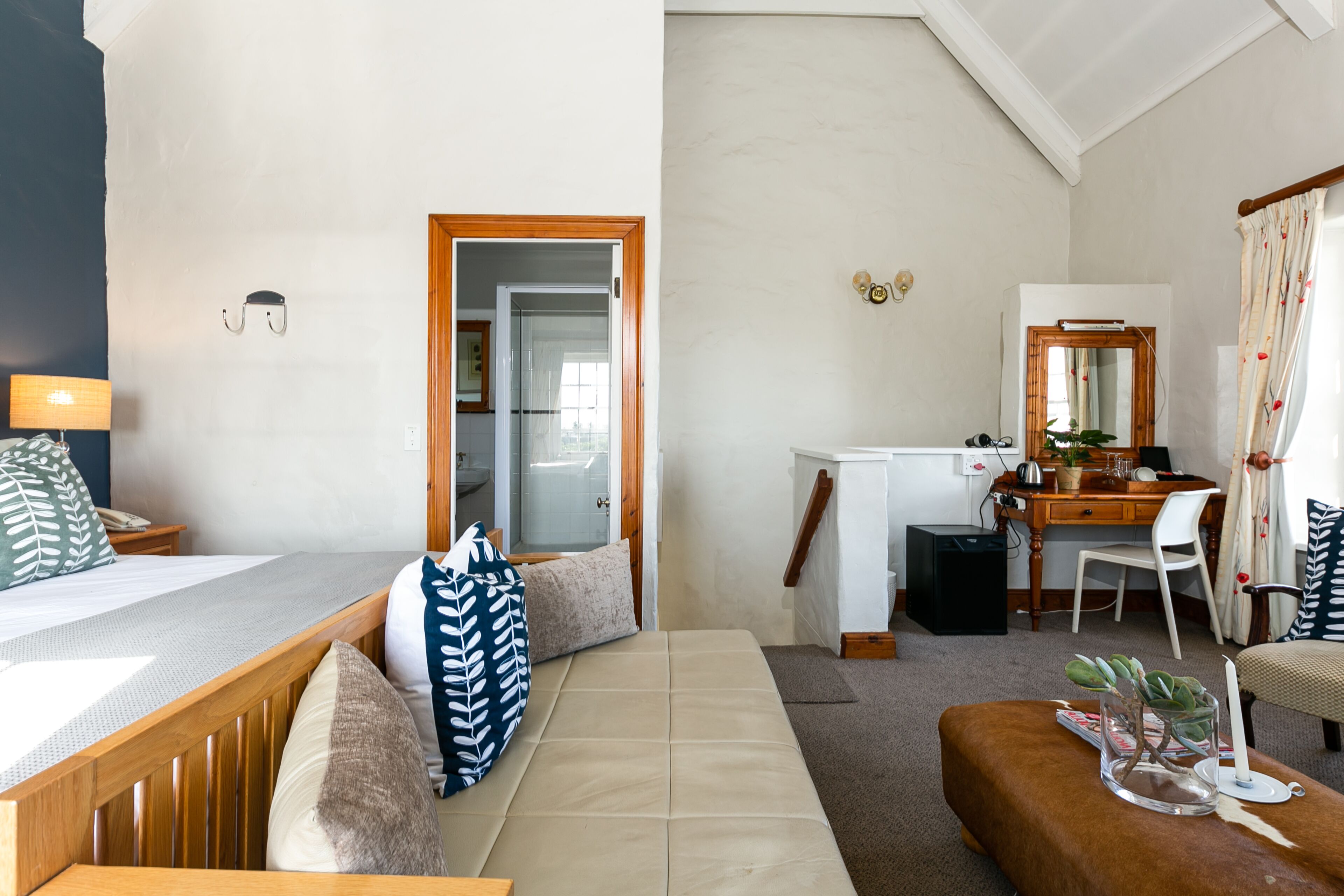 A bedroom with a bed, a desk, and a chair. There is a mirror above the desk and a window with curtains.