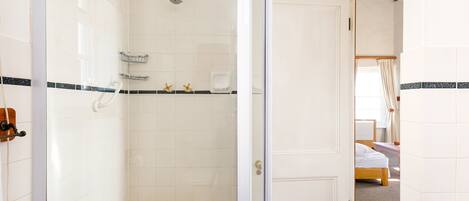 A bathroom with white tiles, a shower, a towel rack, and a door leading to a bedroom.