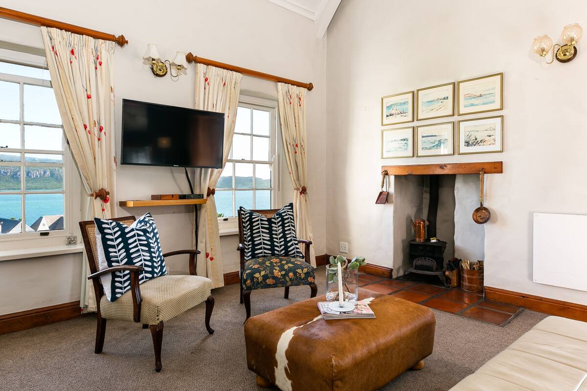 A cozy living room with a fireplace, a television, and a view of the sea.