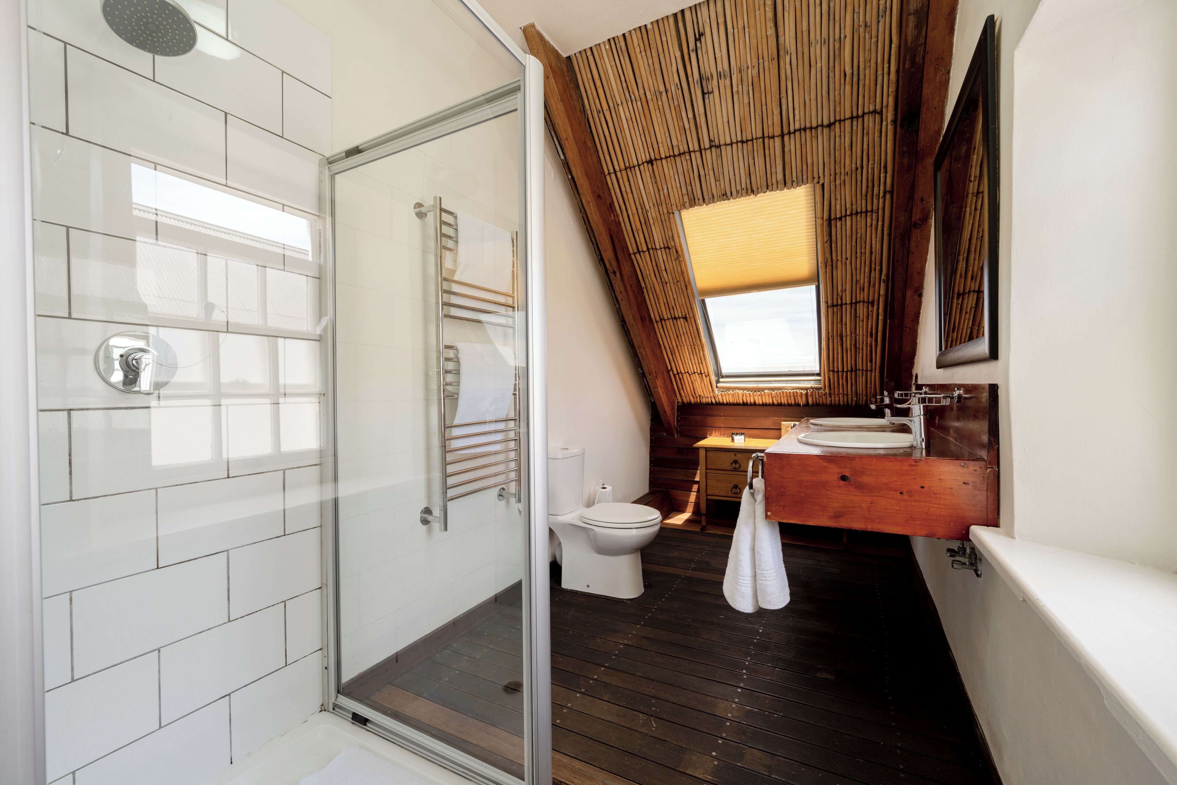 A modern bathroom with a glass shower enclosure, a toilet, and a wooden vanity with a sink and mirror.