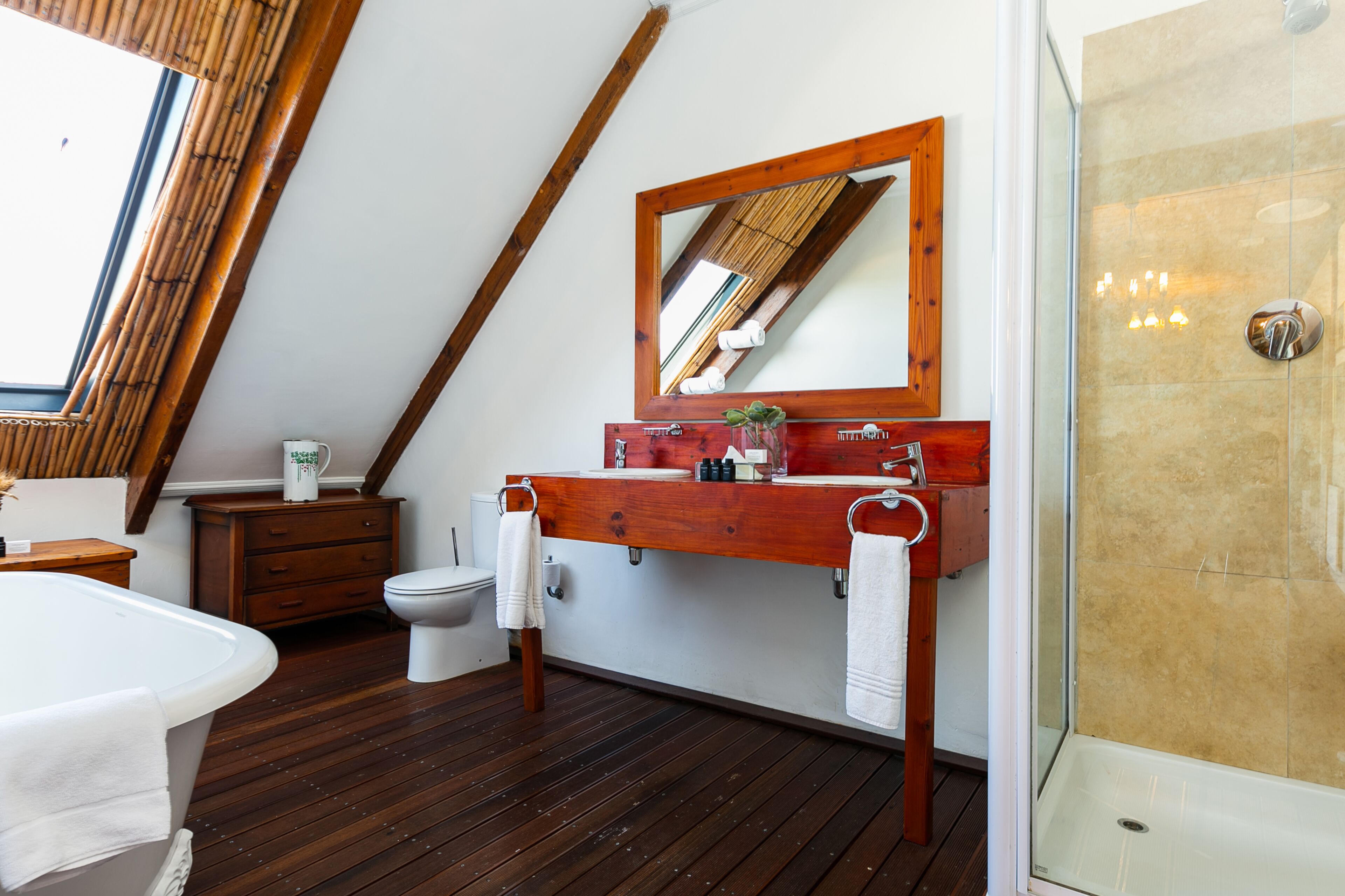A bathroom with a wooden floor, a wooden vanity, a white bathtub, a toilet, a shower, and a skylight.