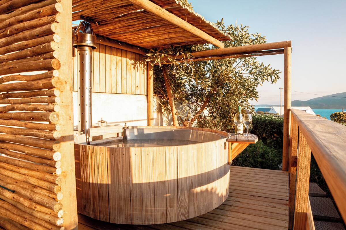 A wooden hot tub with a wooden deck, a wooden pergola, and a view of the sea.