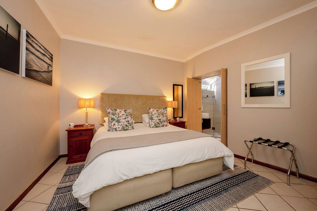A hotel room with a large bed, two bedside tables, a nightstand, a mirror, and a view of a bathroom.