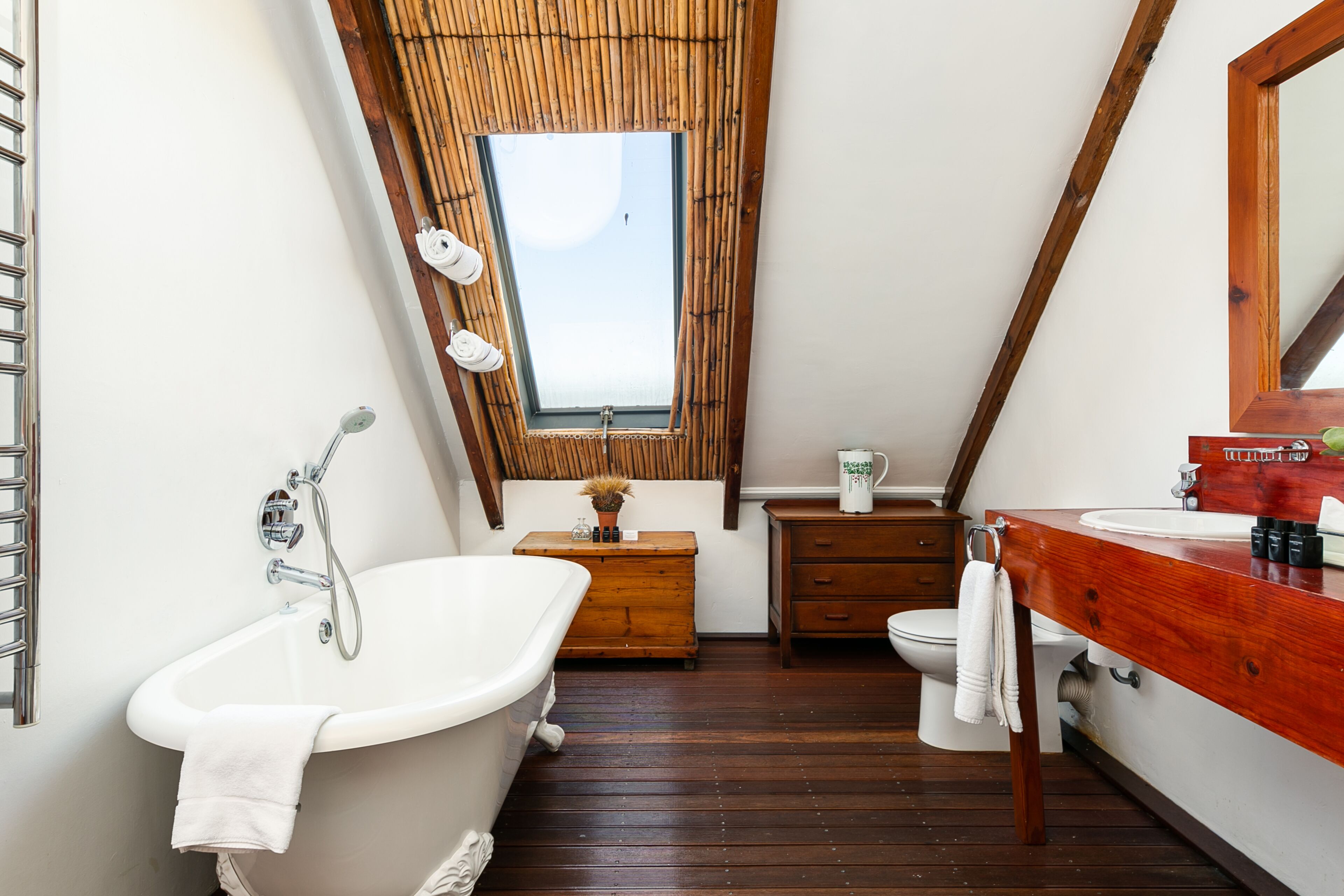 Un baño con suelo de madera, una bañera blanca, un tocador de madera, un inodoro y un tragaluz.