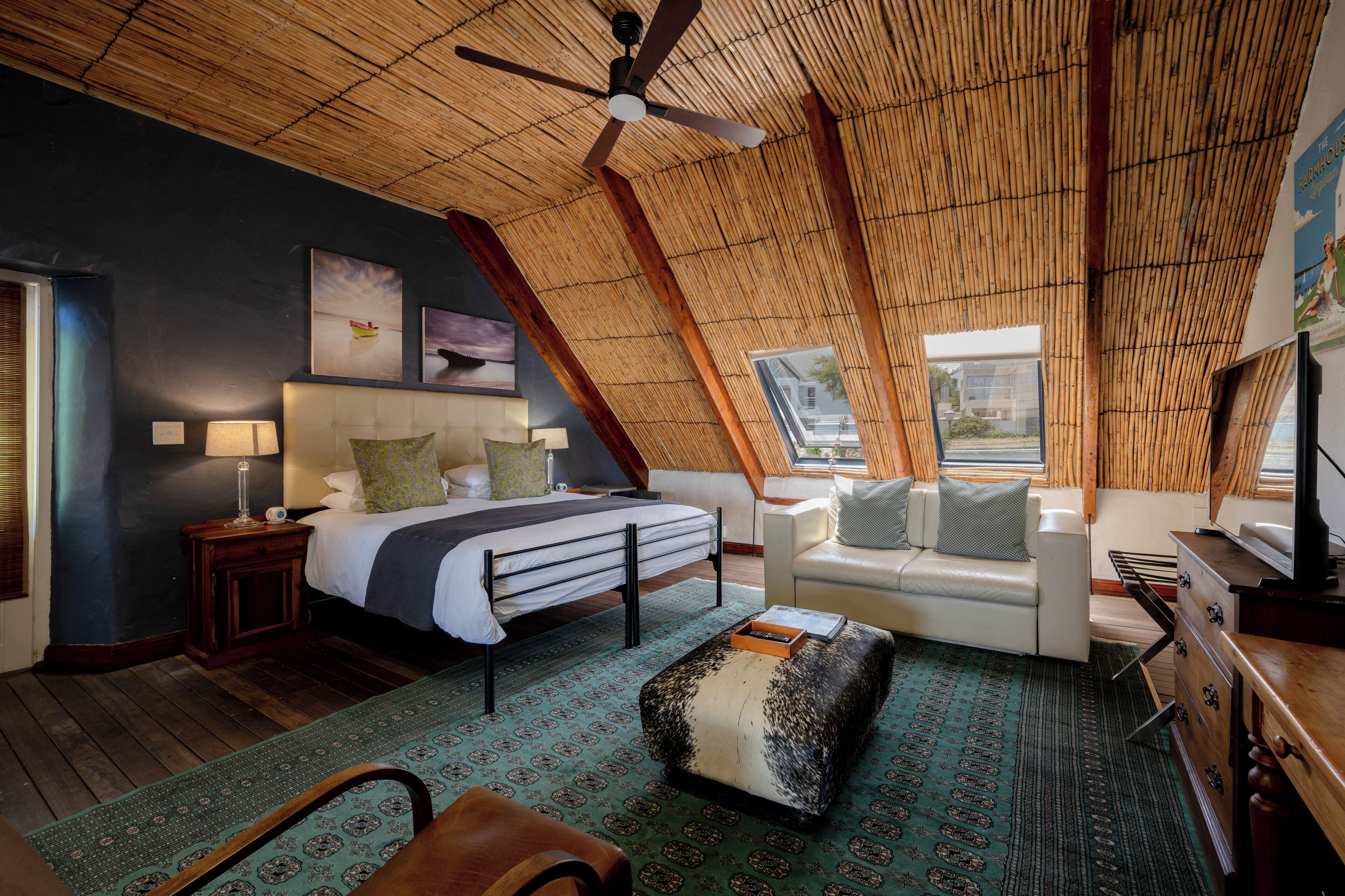 A bedroom with a bed, a sofa, a wooden ceiling, and a window.