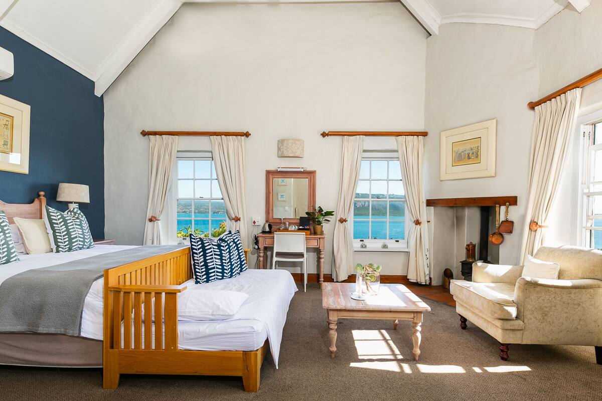 A bedroom with a bed, desk, chair, and a view of the sea.