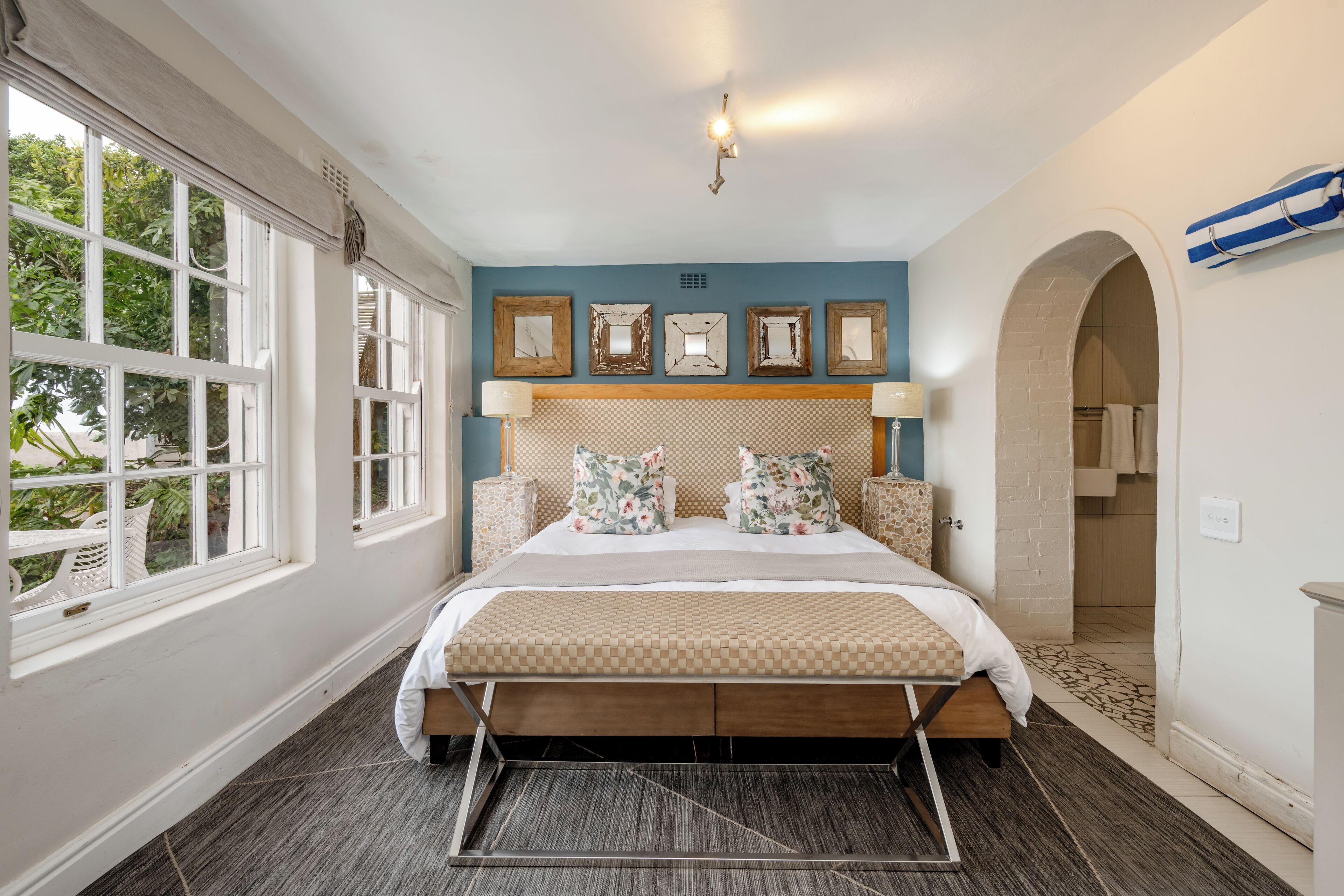 A bedroom with a large bed, a window with curtains, a wall with framed pictures, and a door leading to another room.