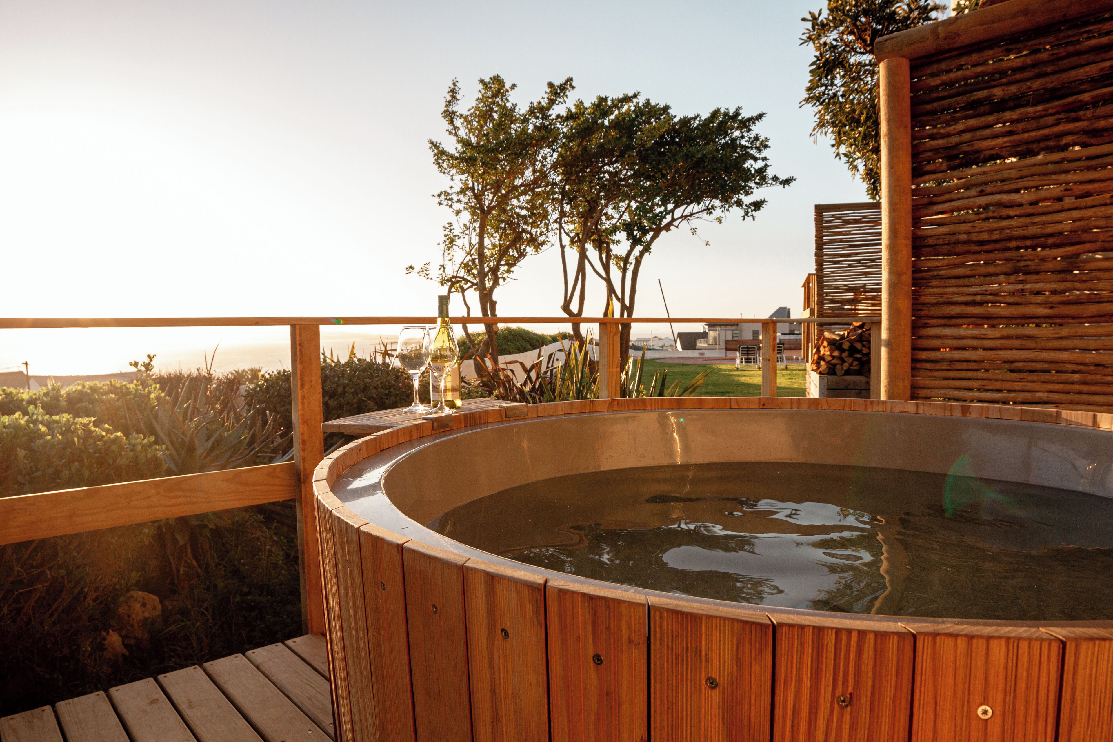 A wooden hot tub on a deck with a view of trees and a distant landscape.