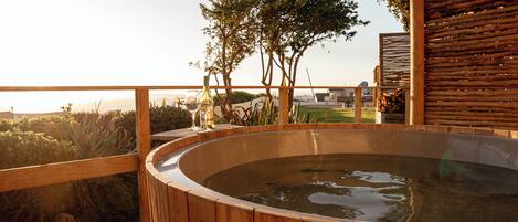 Un jacuzzi de madera en una terraza con vistas a árboles y un paisaje lejano.