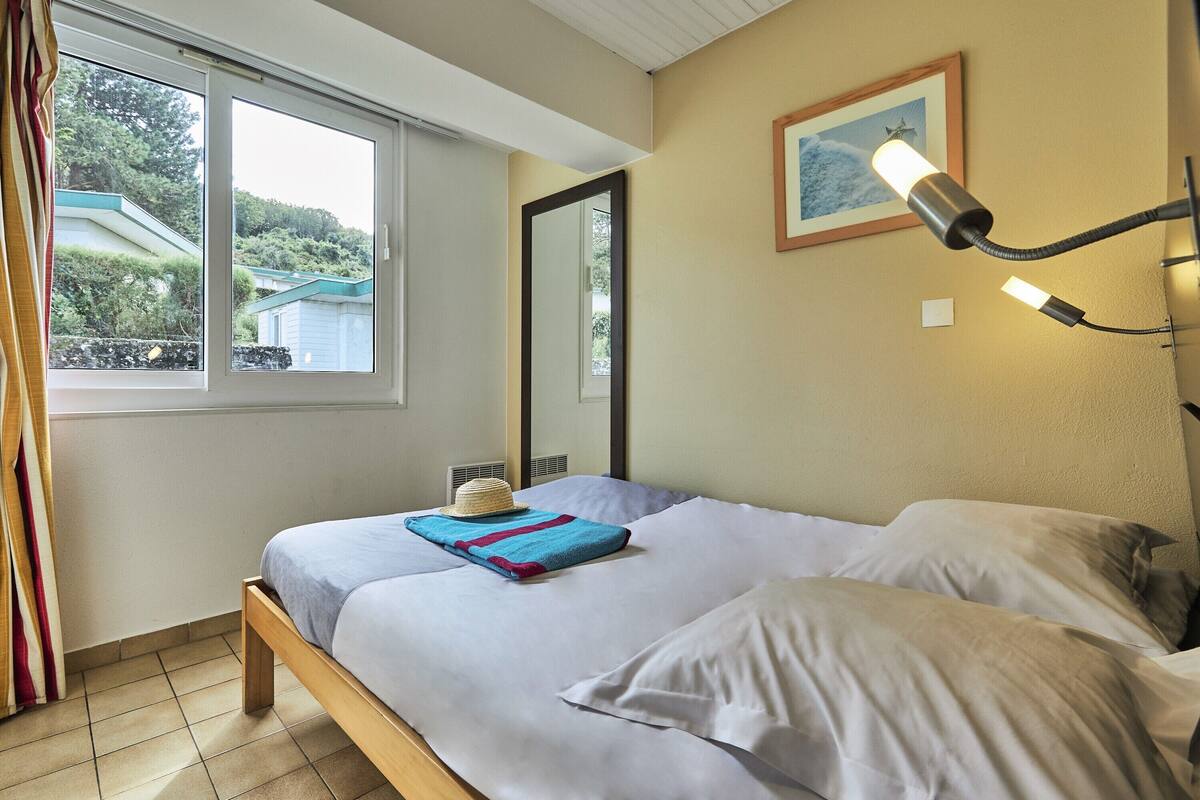 Ein Schlafzimmer mit Bett, Fenster, Wandlampe und einem gerahmten Bild.