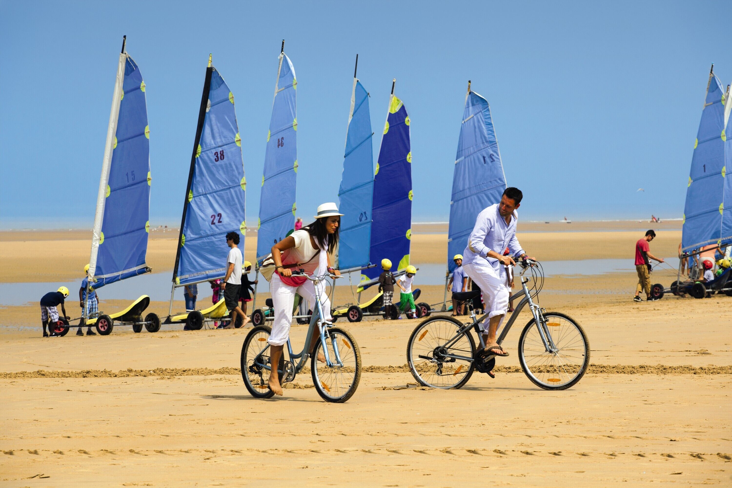 Une plage où l’on voit des gens à vélo et sur des planches à voile.