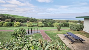 A picnic table and bench in a landscaped garden with a view of the sea.