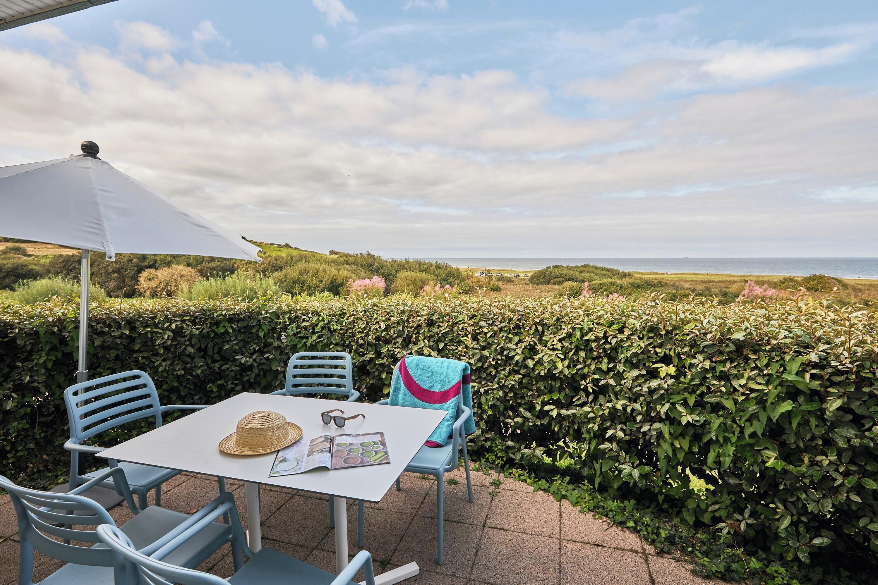 Une terrasse avec une table et des chaises, un parasol blanc et une vue sur la mer.