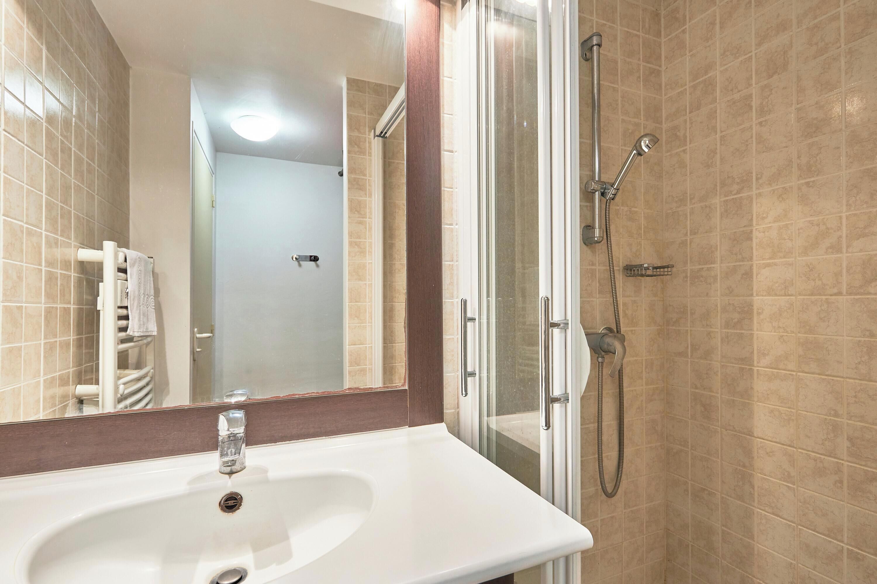 A bathroom with a white sink, a glass shower enclosure, and beige tiled walls.