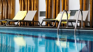 A swimming pool with lounge chairs and a wooden wall in the background. - Hotel Ponta Delgada (Ponta Delgada)