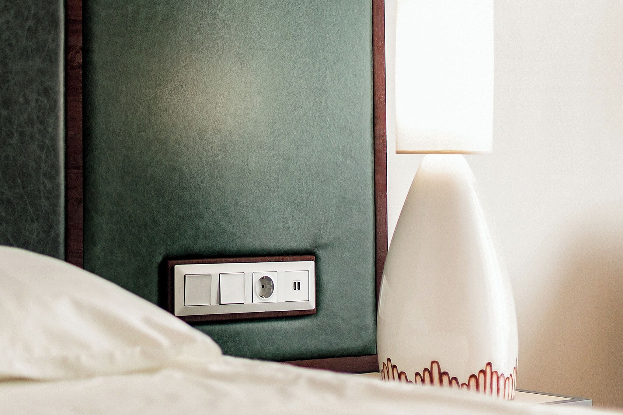 A hotel room with a bed, a bedside lamp, and a wall socket.