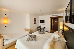 Habitación de hotel con dos camas individuales, un escritorio con silla, un televisor y una puerta que da a otra habitación.
