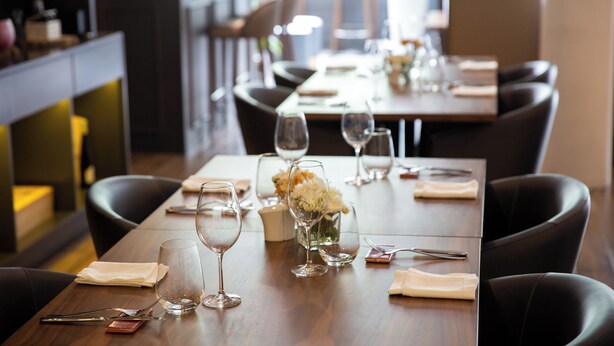 A restaurant setting with a long table set for dining, including wine glasses, cutlery, and a vase with flowers. - Hotel Ponta Delgada (Ponta Delgada)