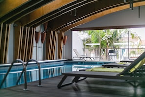 Piscina interior con vistas a palmeras y sillas de descanso.