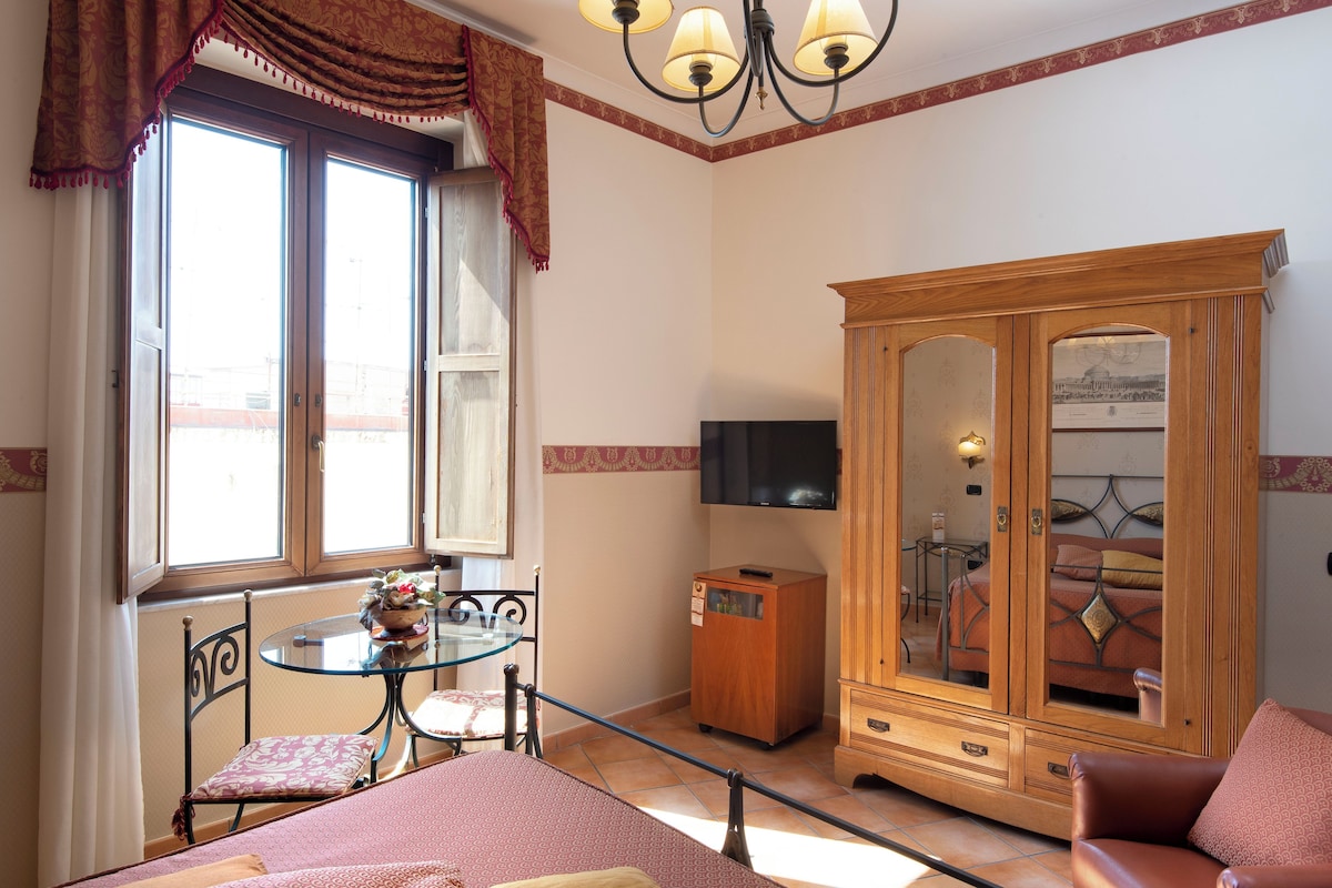 A room with a bed, a wooden cabinet, a television, and a small table with a chair.