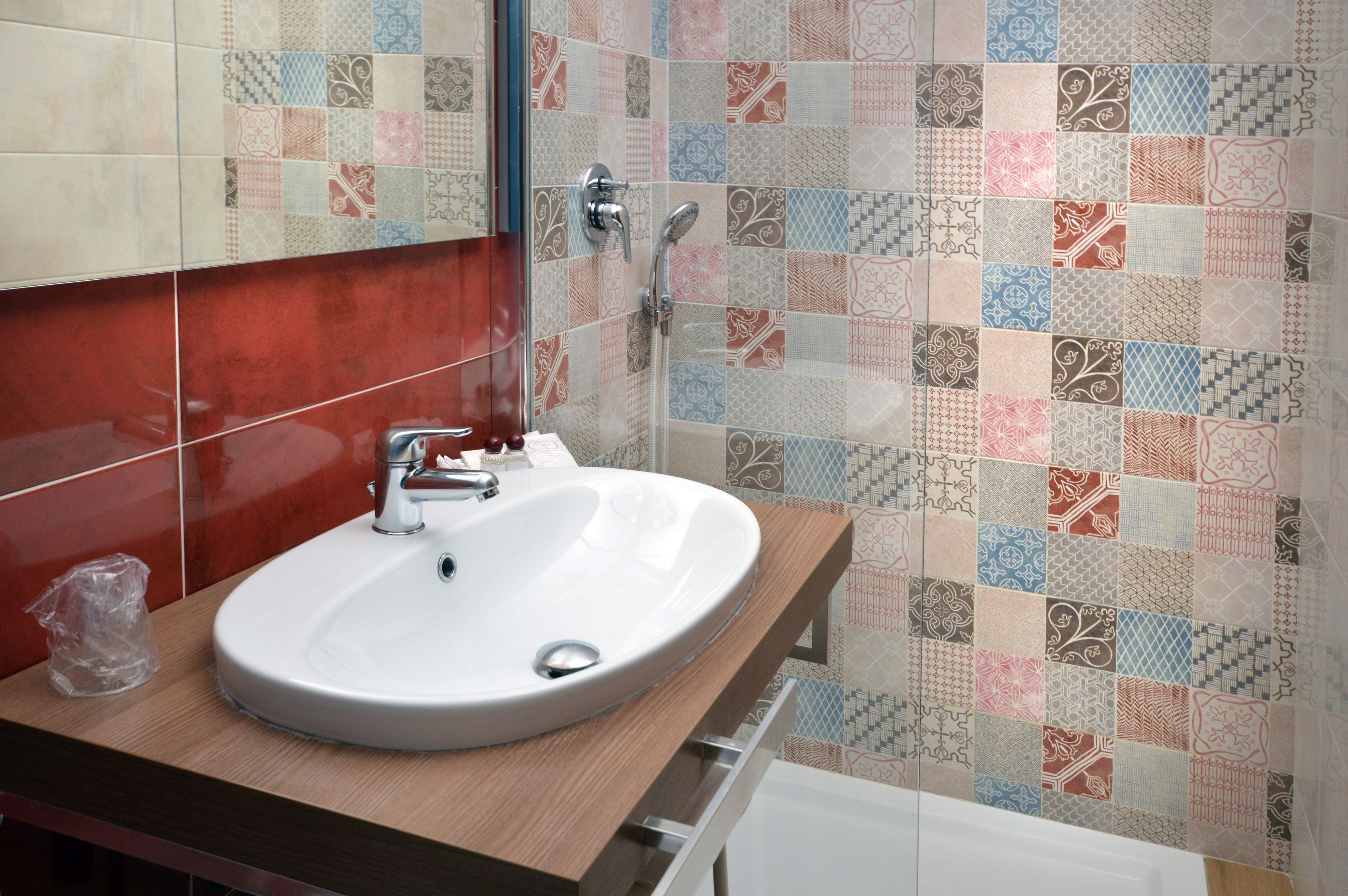 A bathroom with a white sink, a wooden countertop, and a shower with a patterned tile wall.